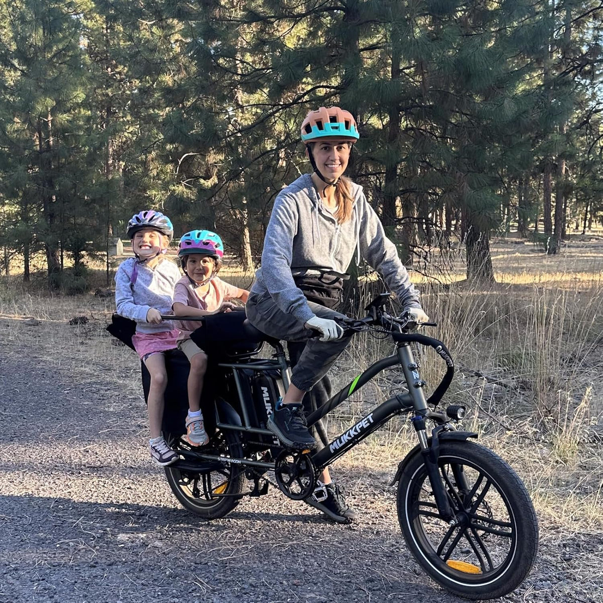 Woman and two children riding a black electric bike in a forested area